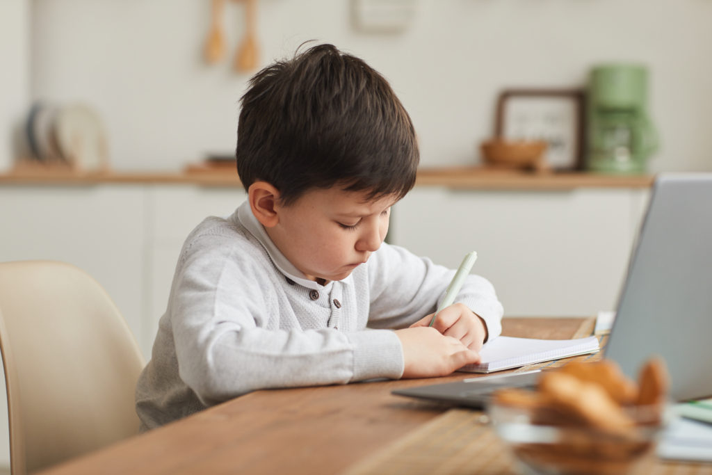 Warm-toned portrait of cute boy writing in notebook