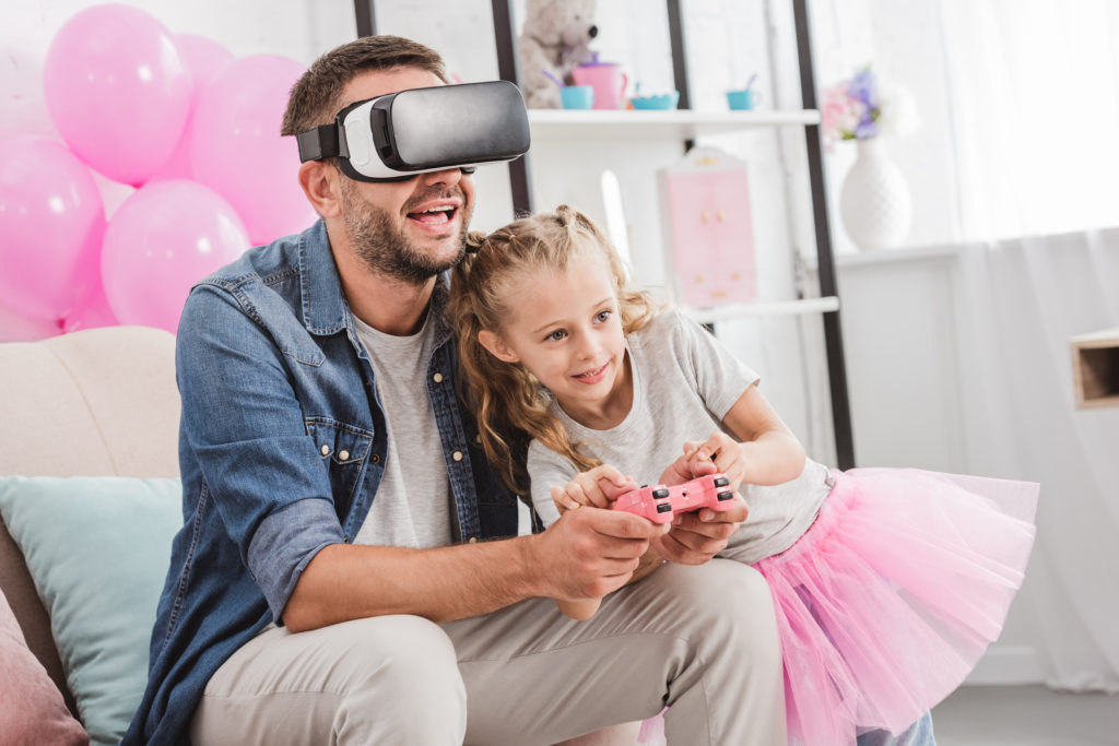 cheerful dad and daughter having fun and playing with joystick and using virtual reality headset on