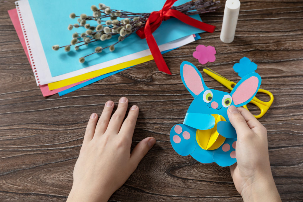 A child is holding an Easter bunny toy card with easter egg. Handmade. Project of childrens creativity, handicrafts, crafts for kids.