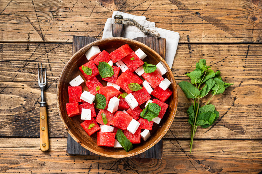 Summer Watermelon Salad with feta cheese and mint in a wooden plate. Wooden background. Top view.