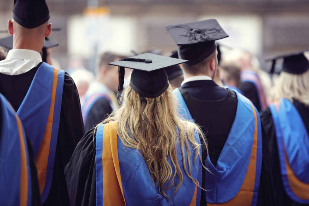 Graduates at university graduation ceremony wearing mortarboard and gown